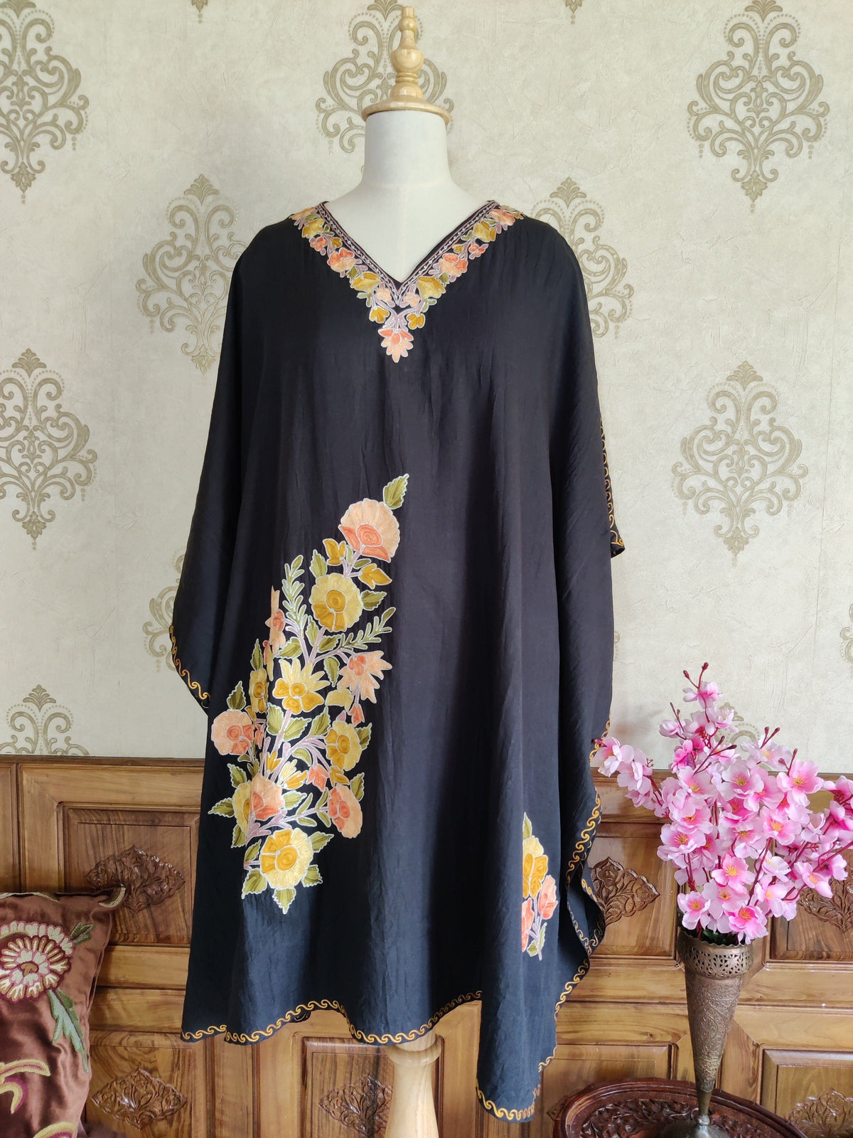 Full front of a black kaftan with yellow and peach Aari flowers, a floral V-neck and wide draped sleeves
