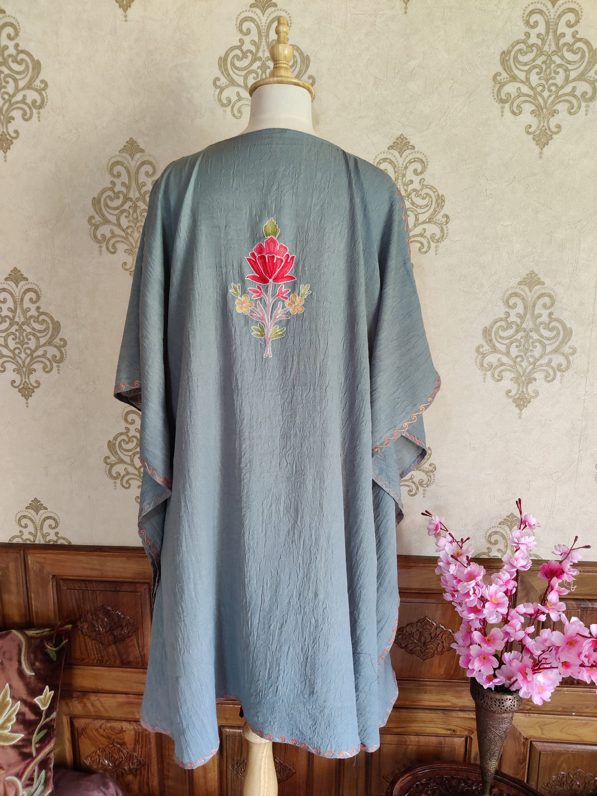 Back of a grey kaftan with a small pink and peach embroidered bouquet high between the shoulders
