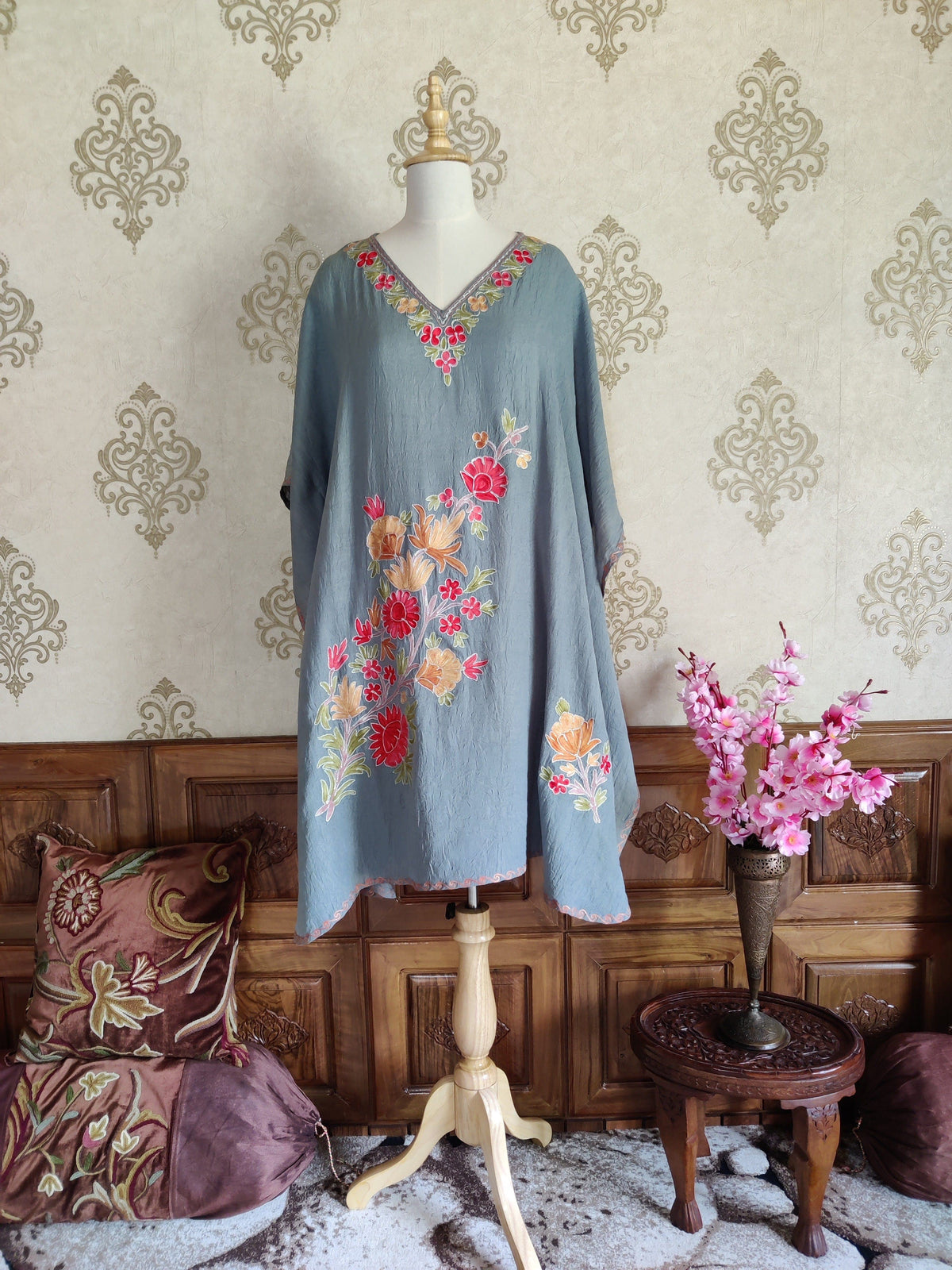 Full front view of a grey kaftan with wide draped sleeves, pink and peach floral embroidery and a V-neck