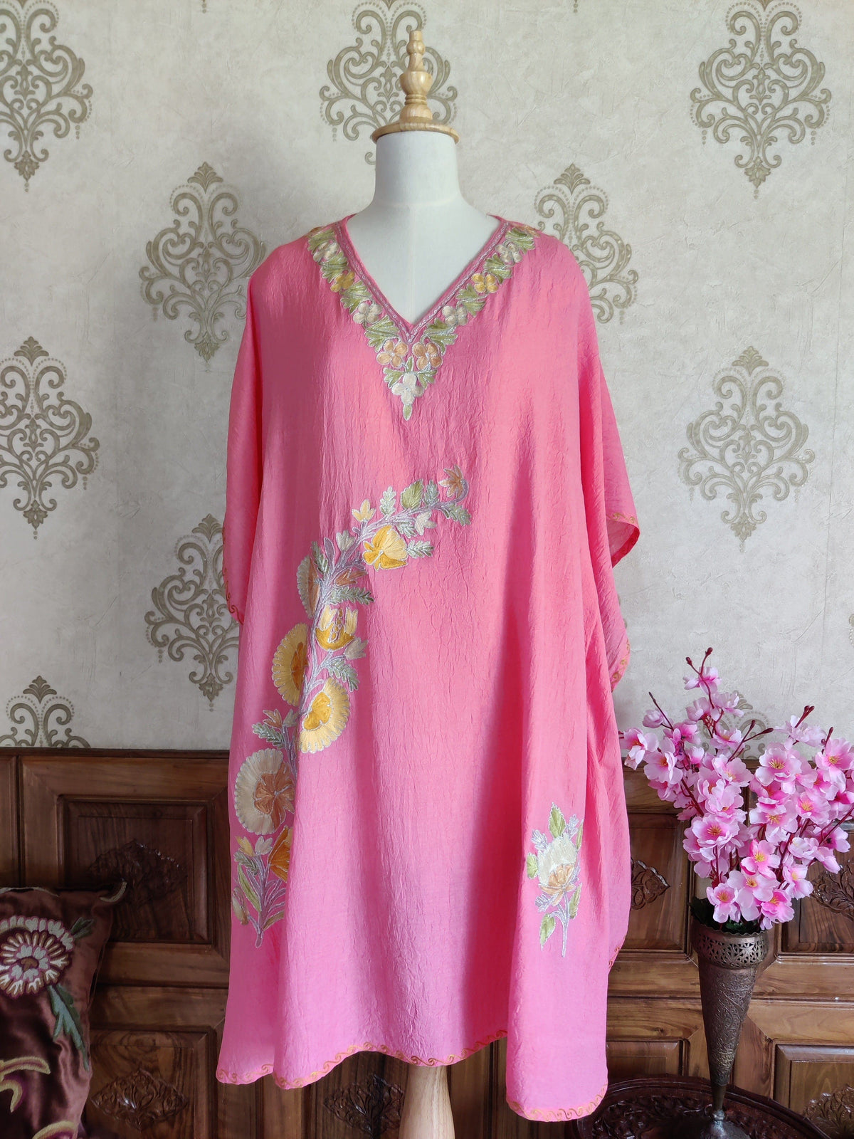 Front view of a pink kaftan, with yellow-and-green floral embroidery at the V-neck, a curved front spray and a smaller motif near the hem.