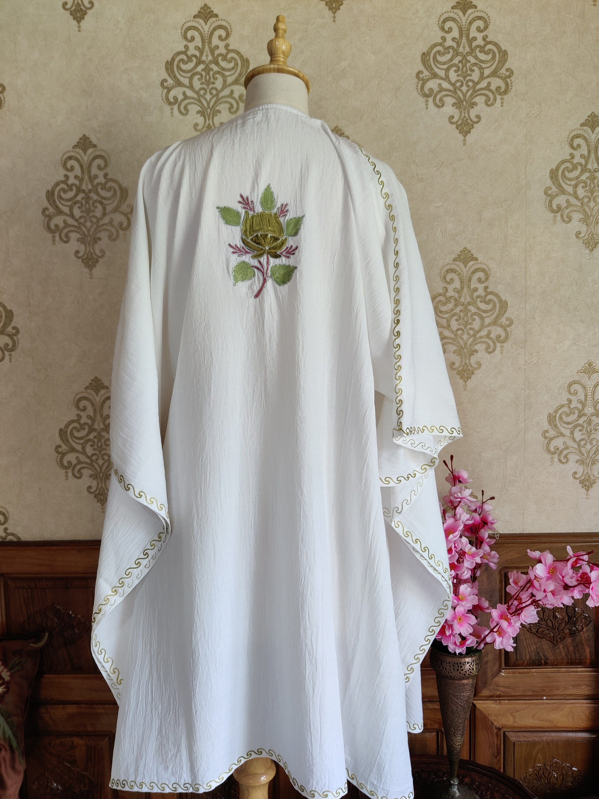 Back of a white kaftan with a small green and mustard floral motif high between the shoulders and narrow embroidered edges.