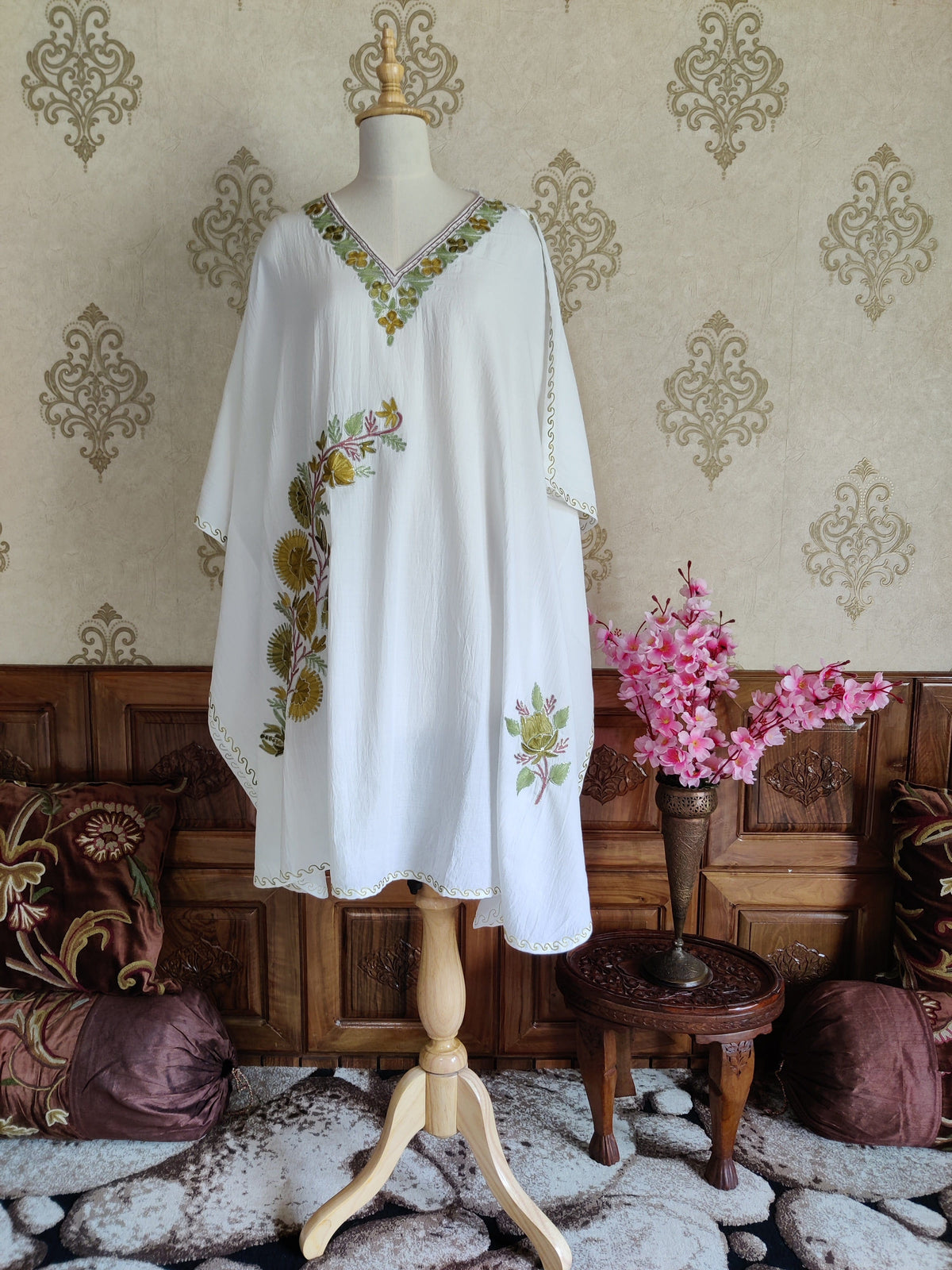 Full front view of a white kaftan with asymmetric floral sprays, wide draped sleeves and narrow embroidered edging.