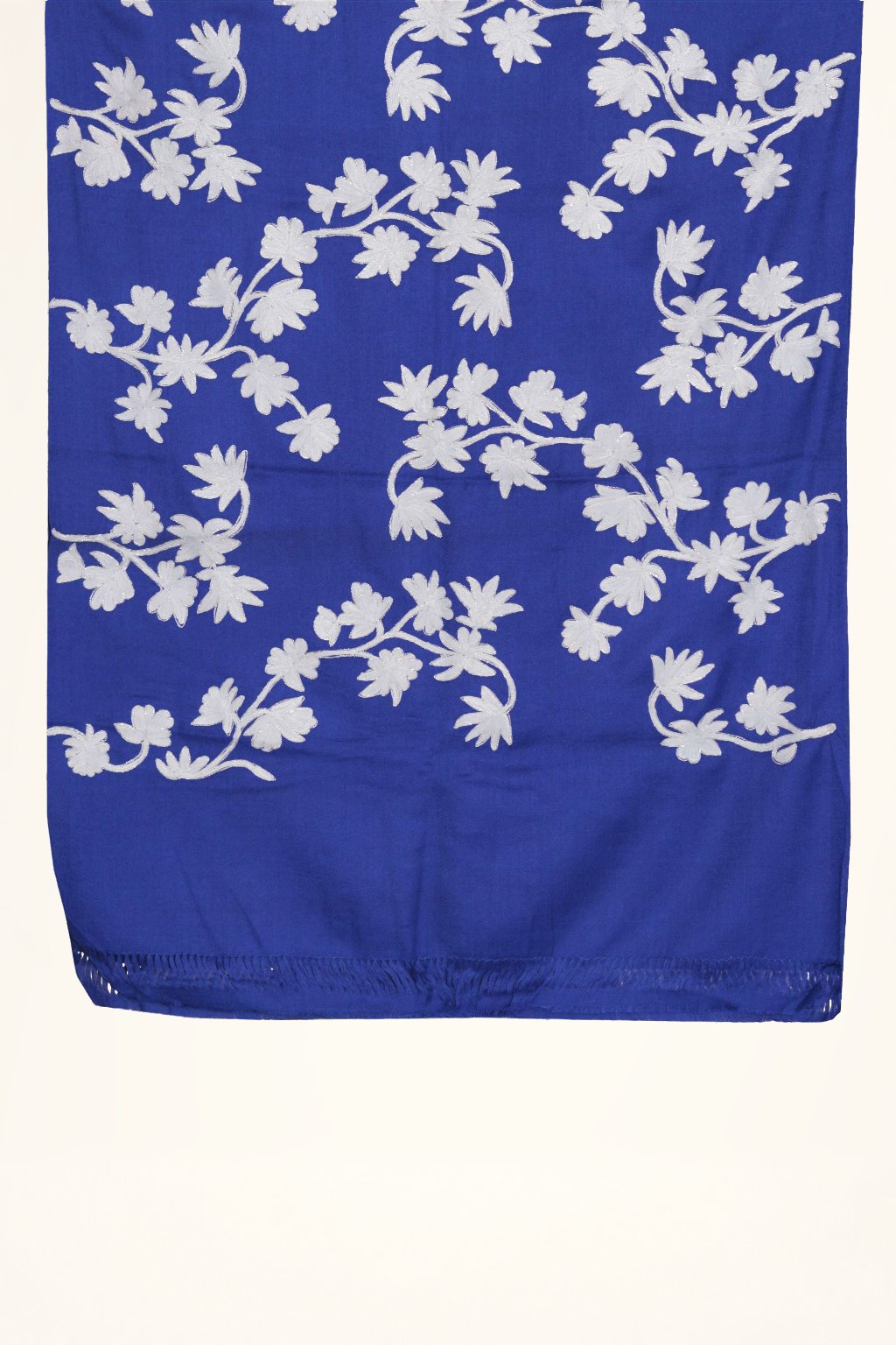 Blue Merino wool stole laid flat, with white Aari floral sprays and curling leaves above a plain fringed end