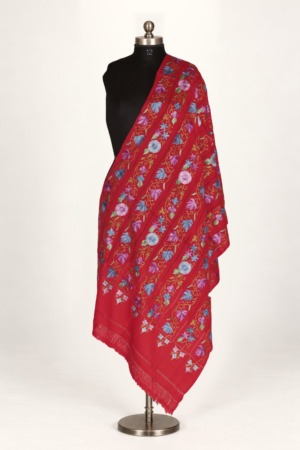 Red-toned Merino wool stole draped on a mannequin, with multicoloured floral Aari cutwork embroidery across the fabric