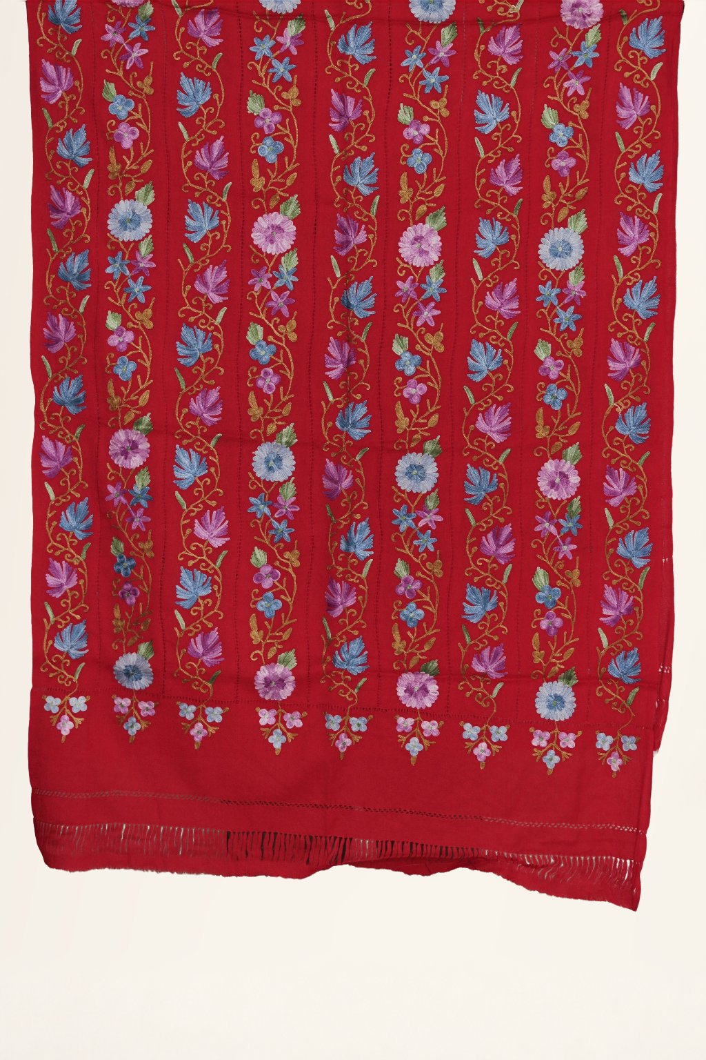 Red-toned Merino wool stole laid flat, with vertical Aari floral vines in blue, pink and green above a narrow fringed end