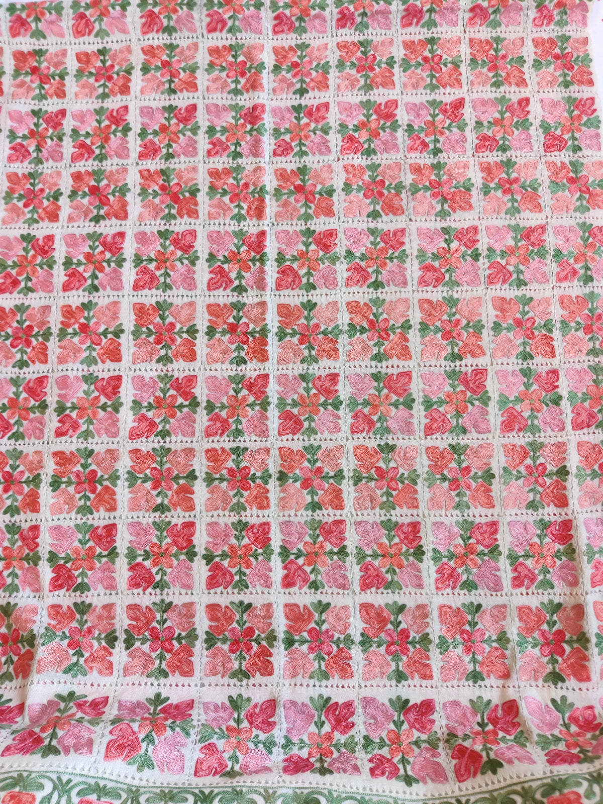 White stole laid flat, showing rows of pink floral squares and an embroidered floral border.