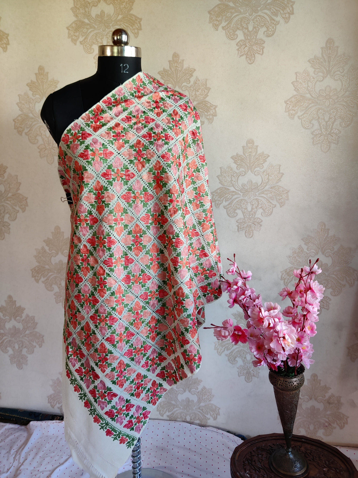 Full view of a white stole draped on a mannequin, covered in pink floral squares with green leaves and openwork lines.