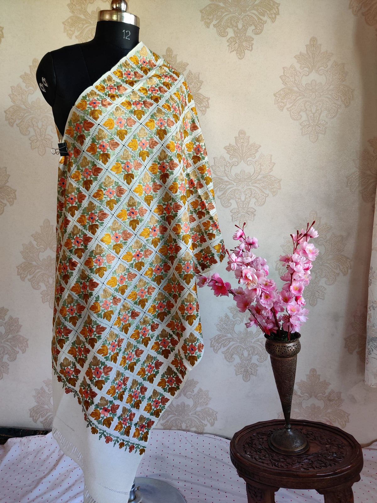 Full-length white Merino wool scarf draped on a mannequin, covered in colourful Aari floral squares and openwork grid lines