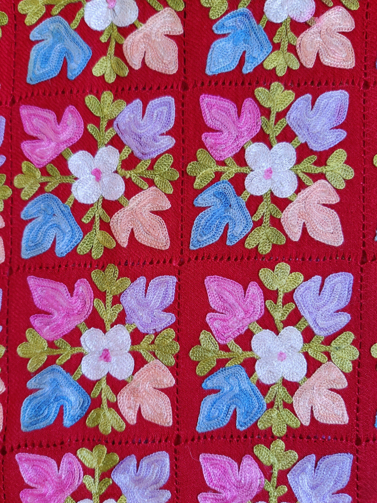 Close-up of blue, pink and lavender leaves around ivory flowers, separated by red cutwork lines.