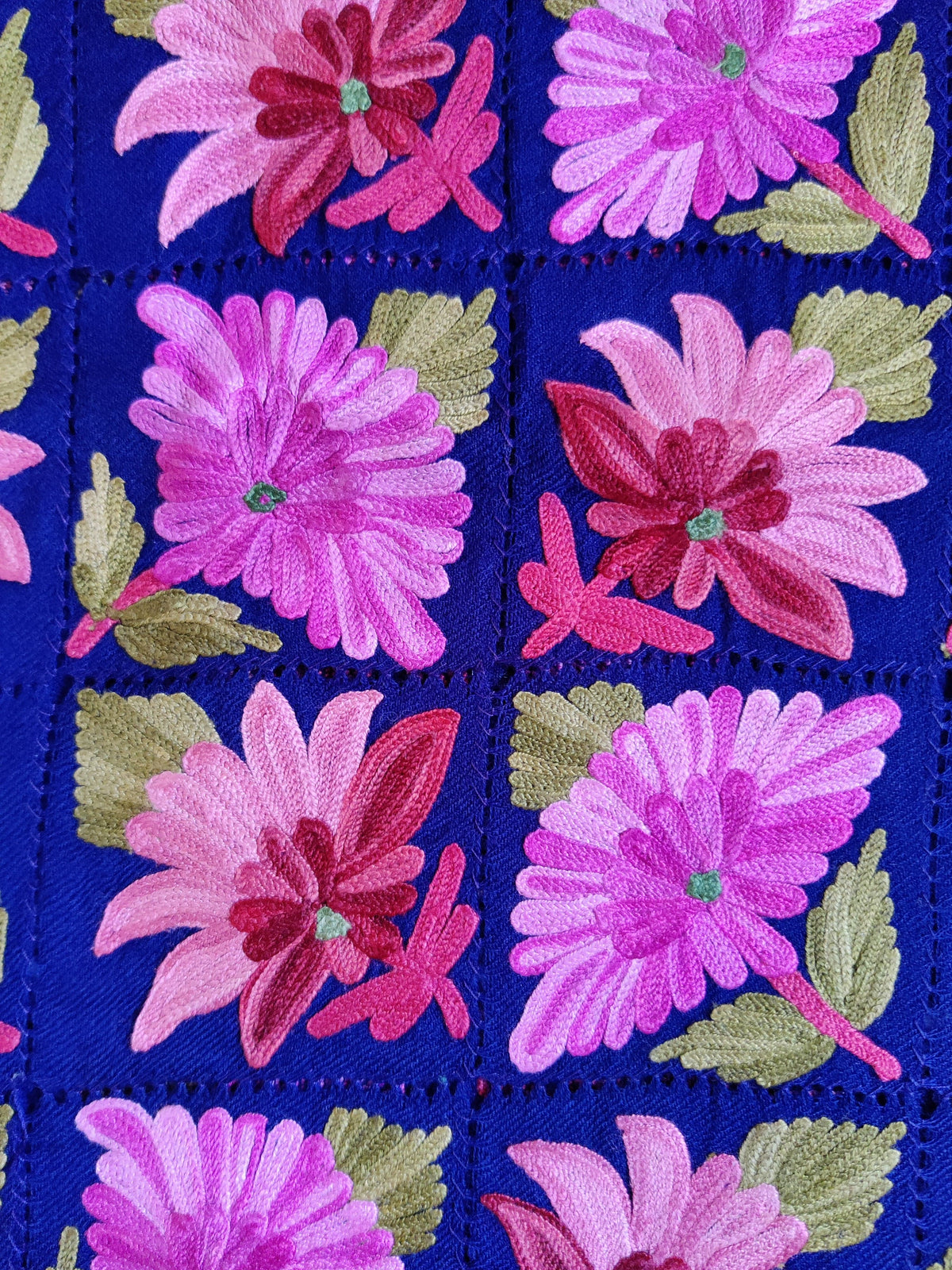 Close-up of alternating pink Aari flowers and green leaves inside openwork squares on royal-blue Merino wool scarf