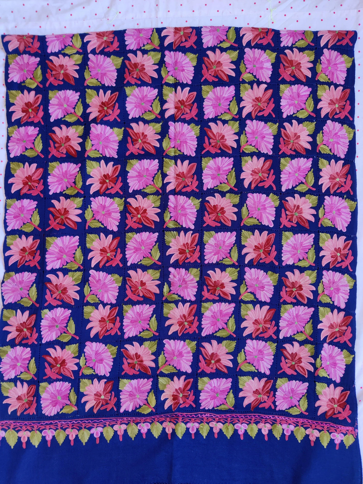 Royal-blue Merino wool scarf spread flat, with pink Aari floral squares, a narrow leafy end border and plain blue strip