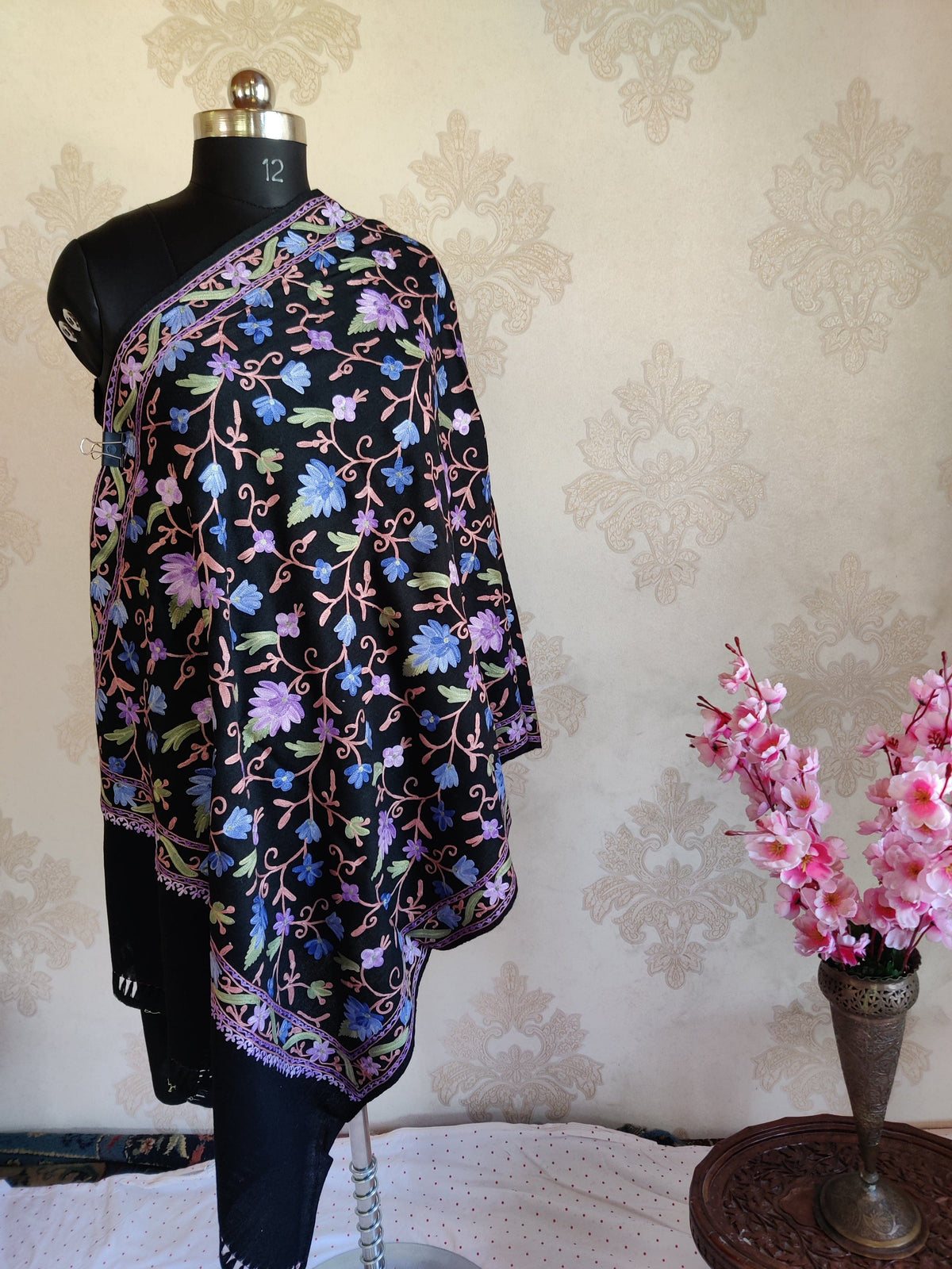 Black merino wool stole draped on a mannequin, with all-over pastel Aari floral vines, a narrow matching border and plain black ends.