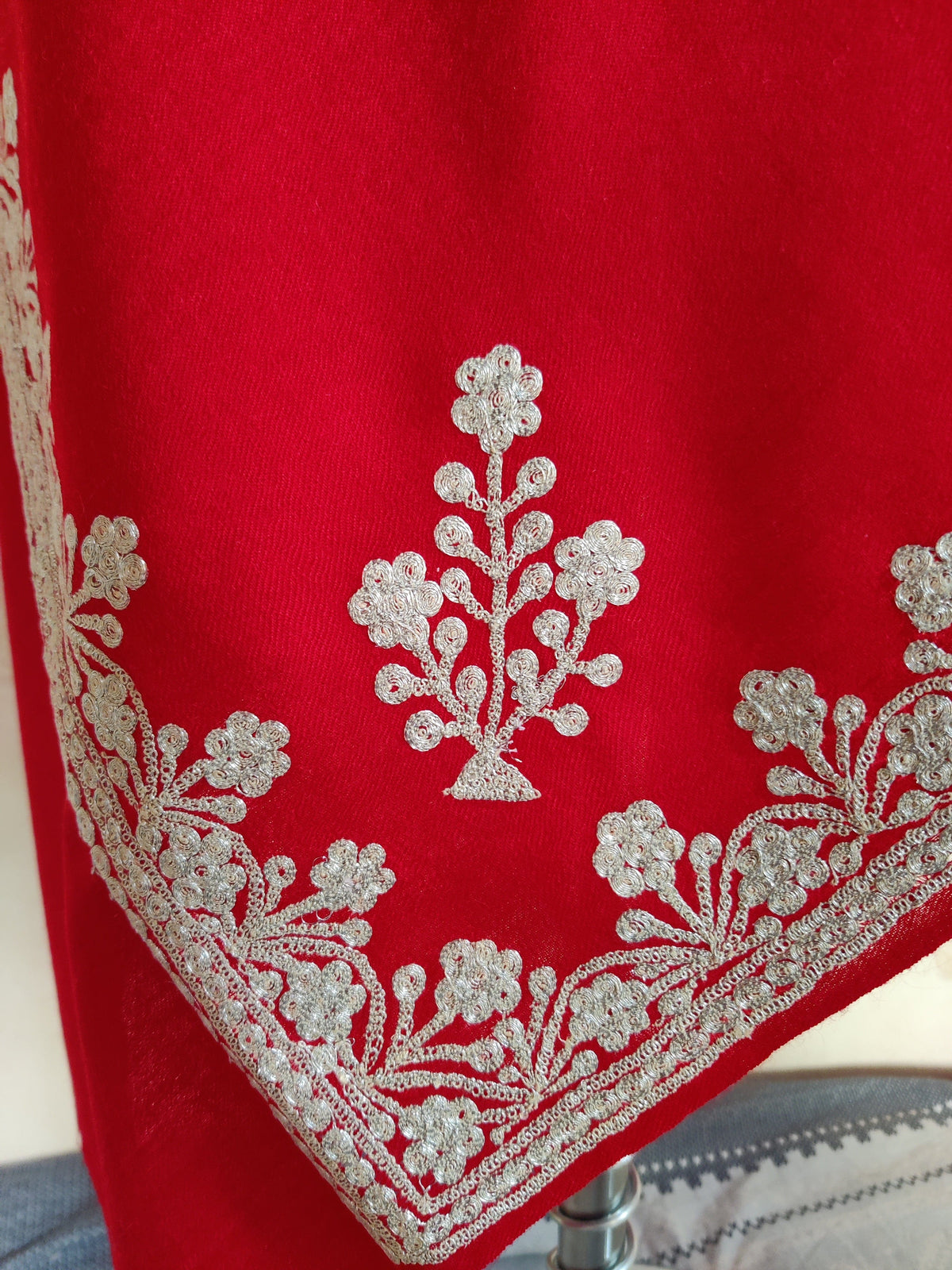 Corner detail of red Merino wool scarf with a silver-toned Tilla flowering sprig above the floral border