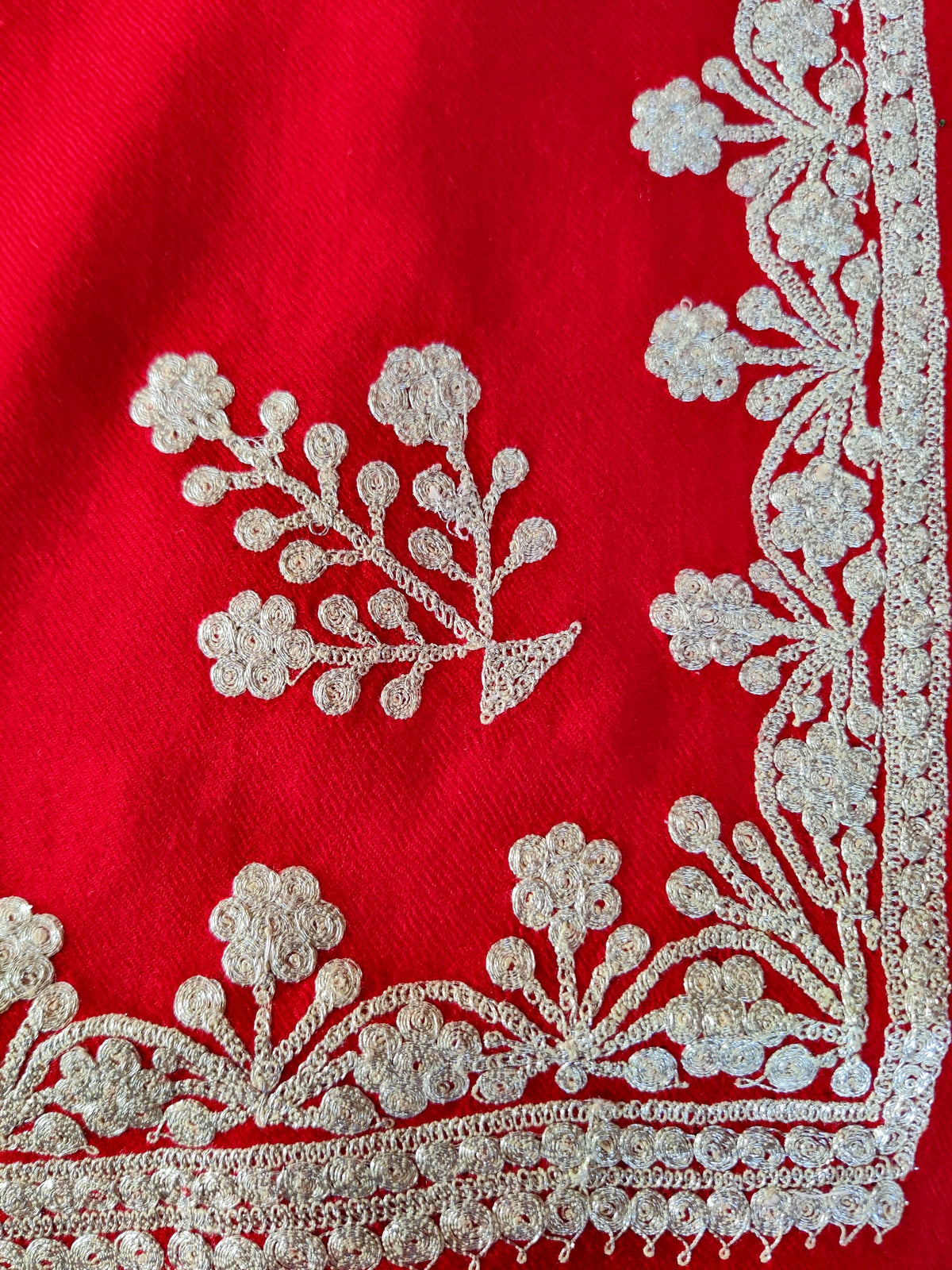 Flat corner detail of red Merino wool scarf showing a silver-toned Tilla floral sprig and matching border