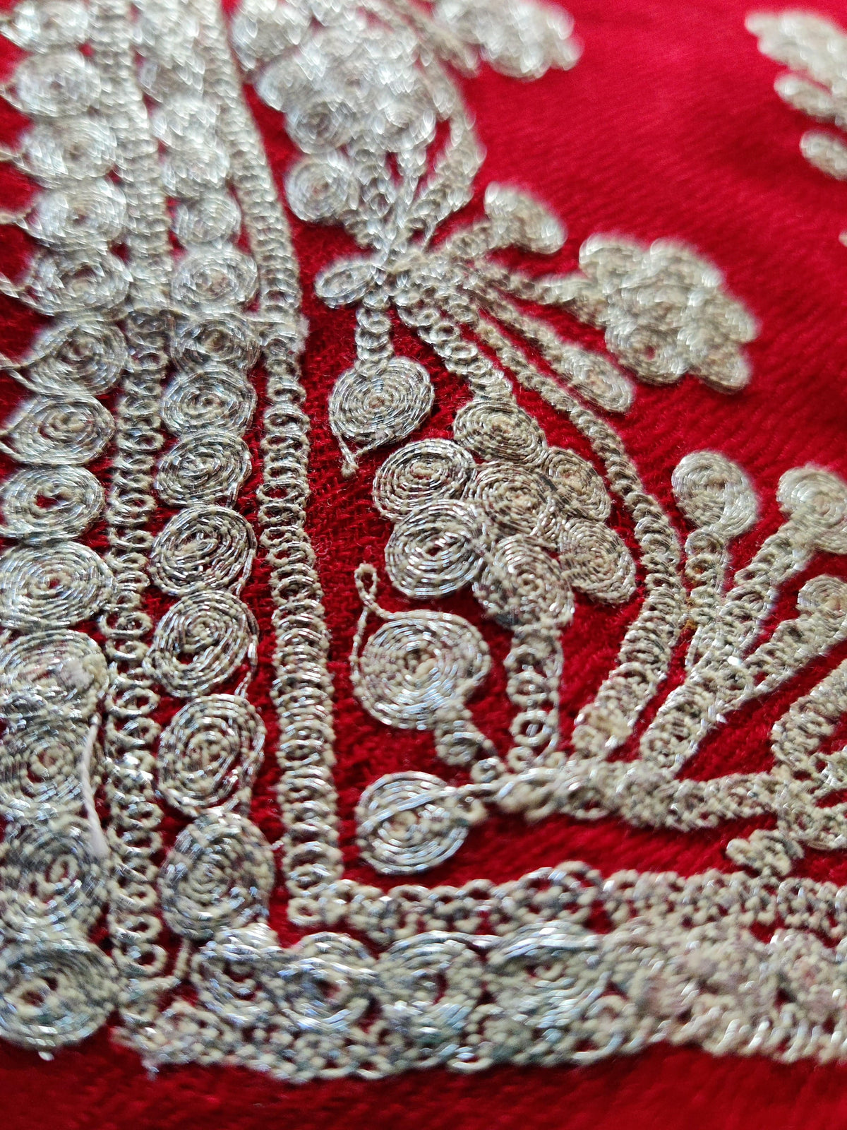 Macro close-up of silver-toned Tilla threadwork forming flowers and curling stems along the red Merino scarf border