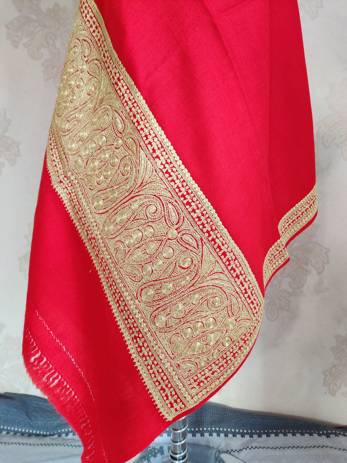 Hanging corner of a red Merino wool stole showing a broad pale-gold Tilla paisley end border and short fringe