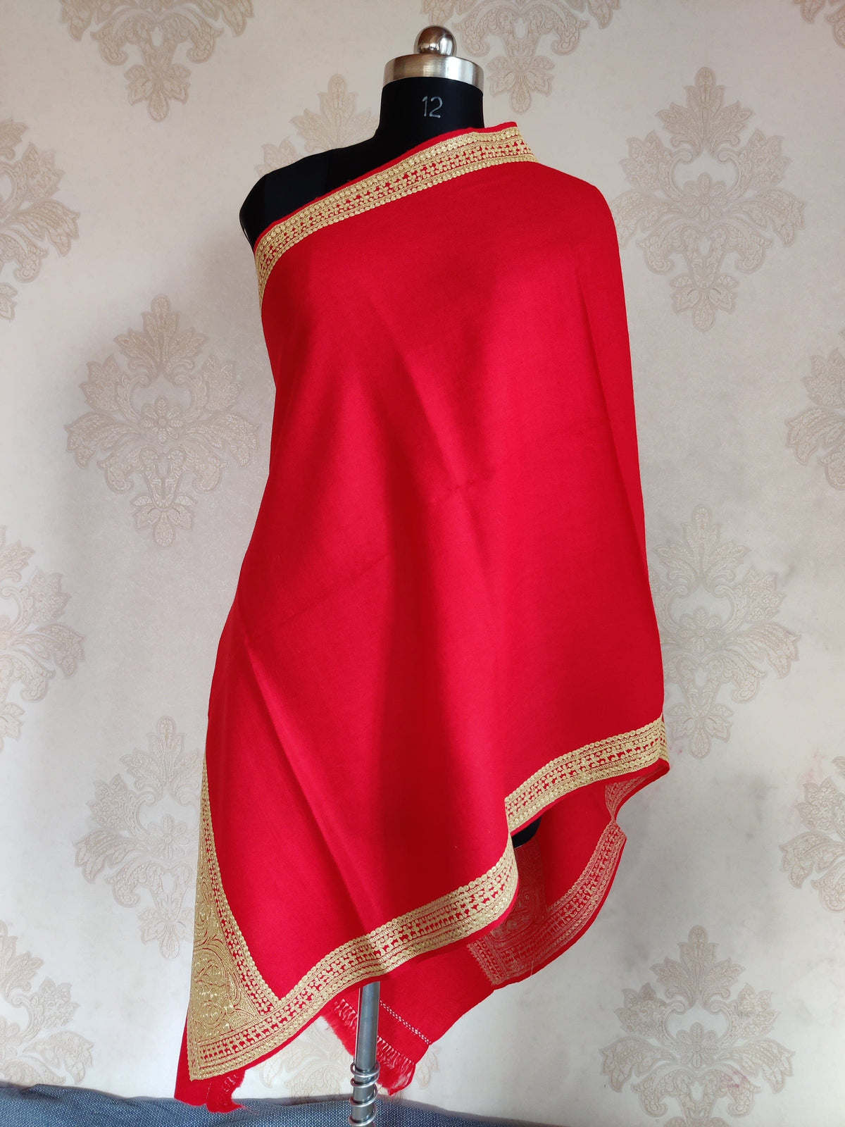 Full view of a red Merino wool stole draped on a mannequin, with a plain centre framed by narrow Tilla borders and a broad embroidered end