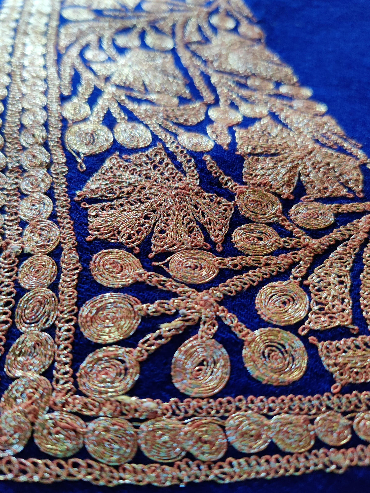 Angled macro view of the blue stole’s textured gold-toned maple leaves and scrolling border.