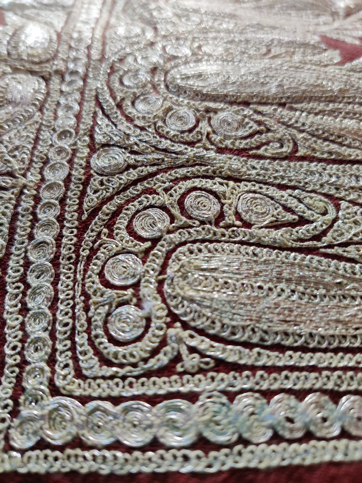 Angled macro view of the reddish-brown stole’s silver-toned paisley embroidery and small scrolling stitches.