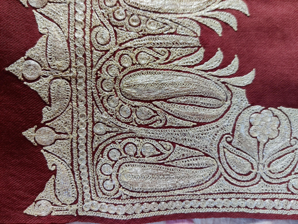 Flat corner close-up of silver-toned paisleys and curling outlines embroidered on reddish-brown fabric.