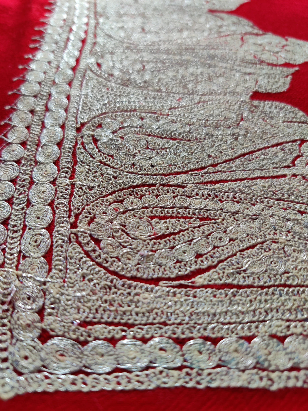 Macro close-up of silver-toned Tilla threadwork in the paisley border of red Merino wool scarf