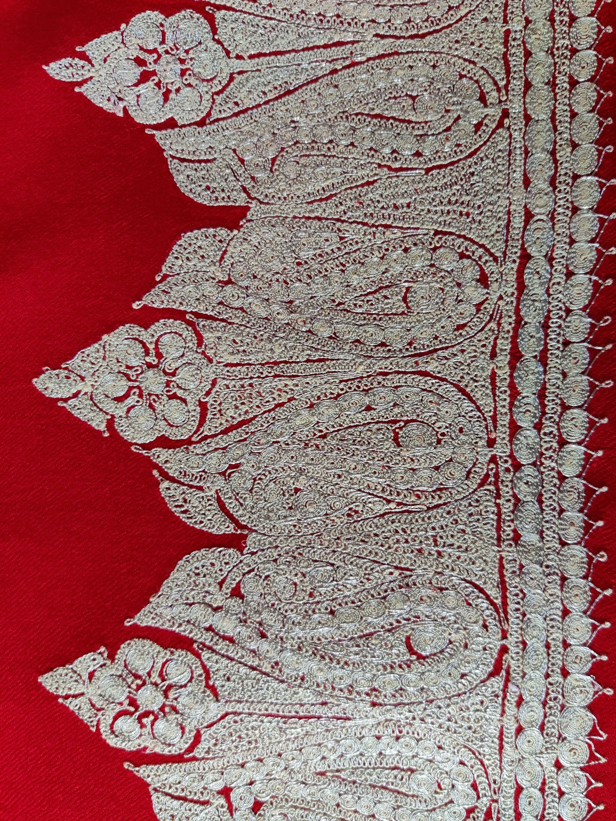 Flat close-up of repeating silver-toned Tilla paisley and floral motifs along the red Merino scarf end border