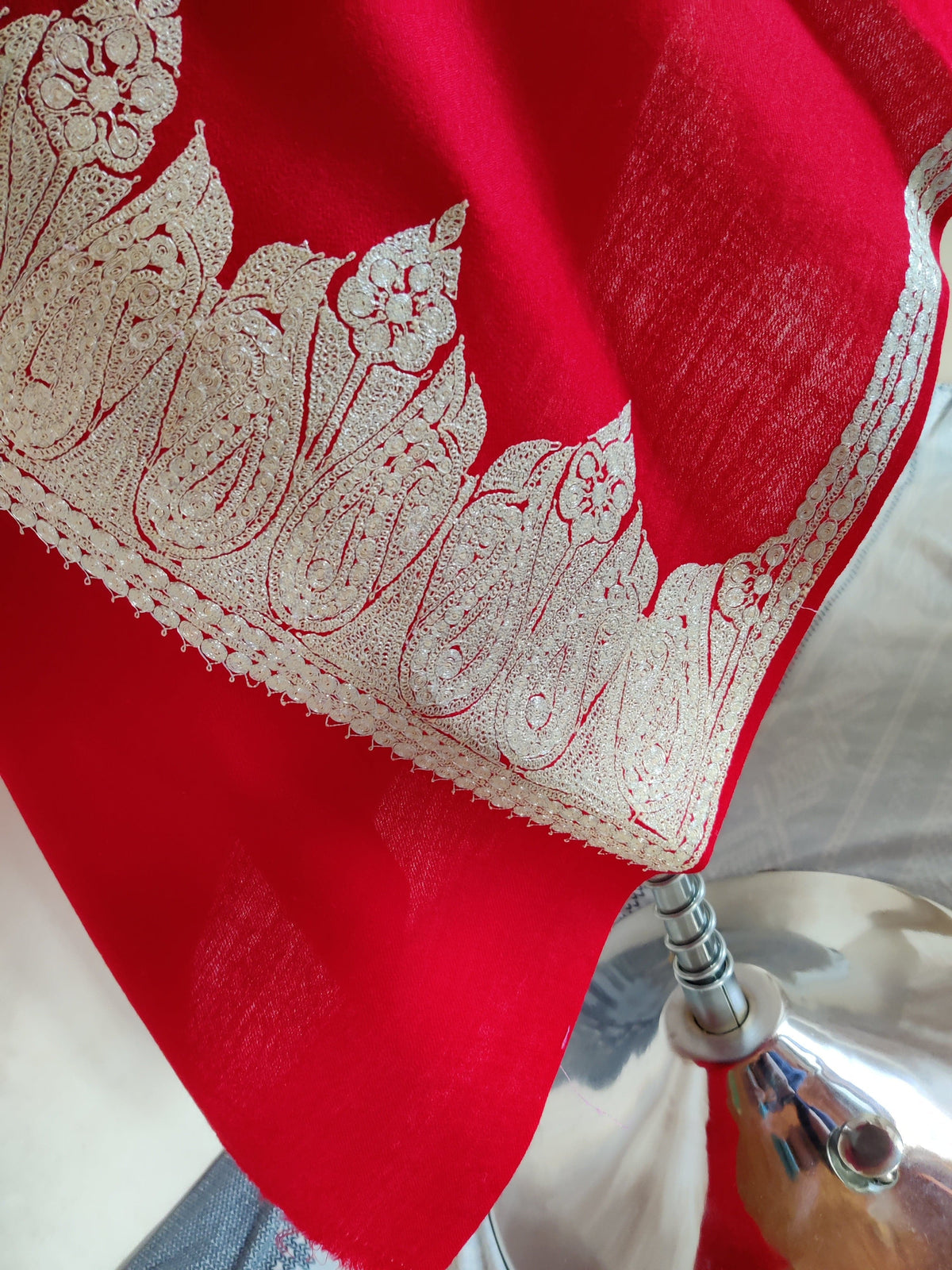 Lower drape of red Merino wool scarf showing a broad silver-toned Tilla paisley end border meeting narrow side trim