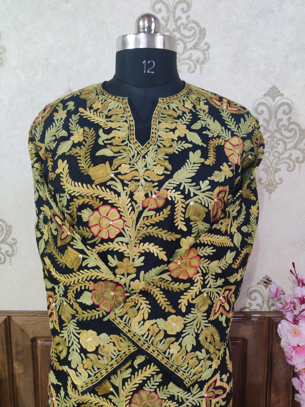 Upper front of a black pheran on a mannequin with crossed sleeves, yellow floral embroidery and a slit neckline.