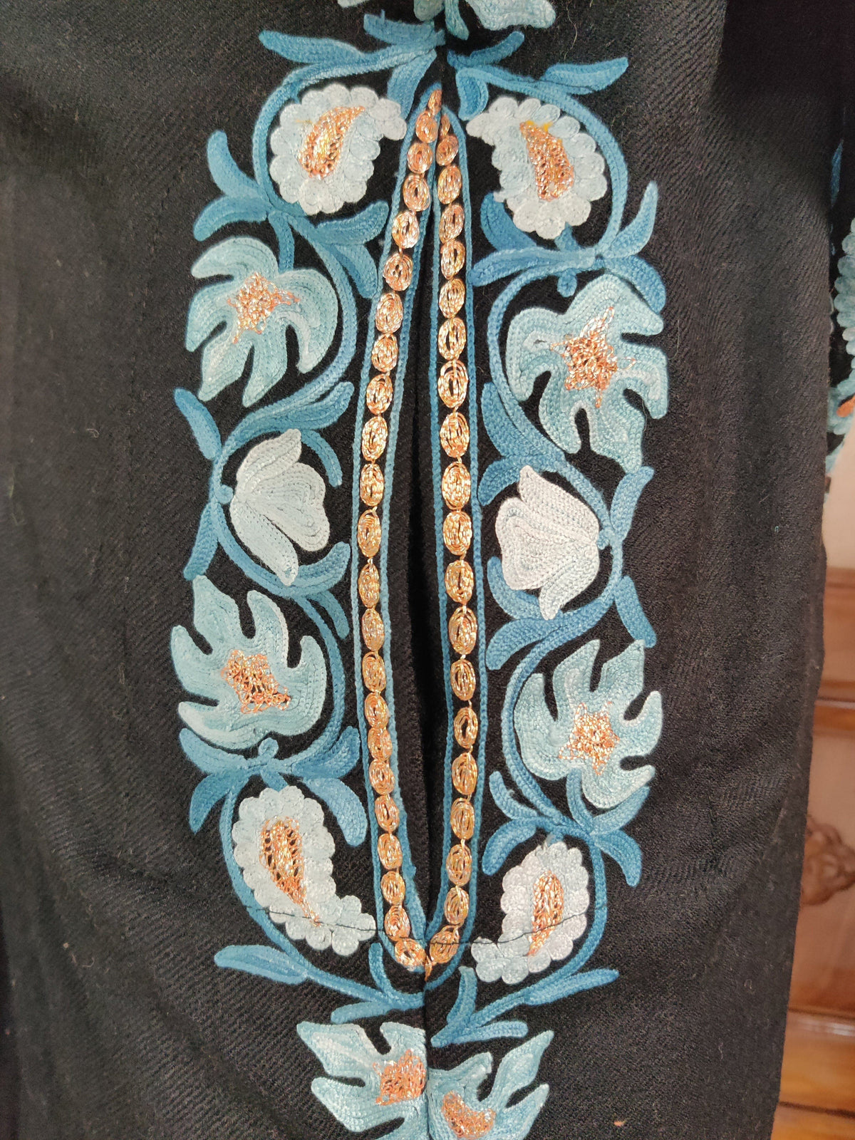 Elongated slit edged with blue and ivory floral embroidery and gold-toned stitching on black fabric.