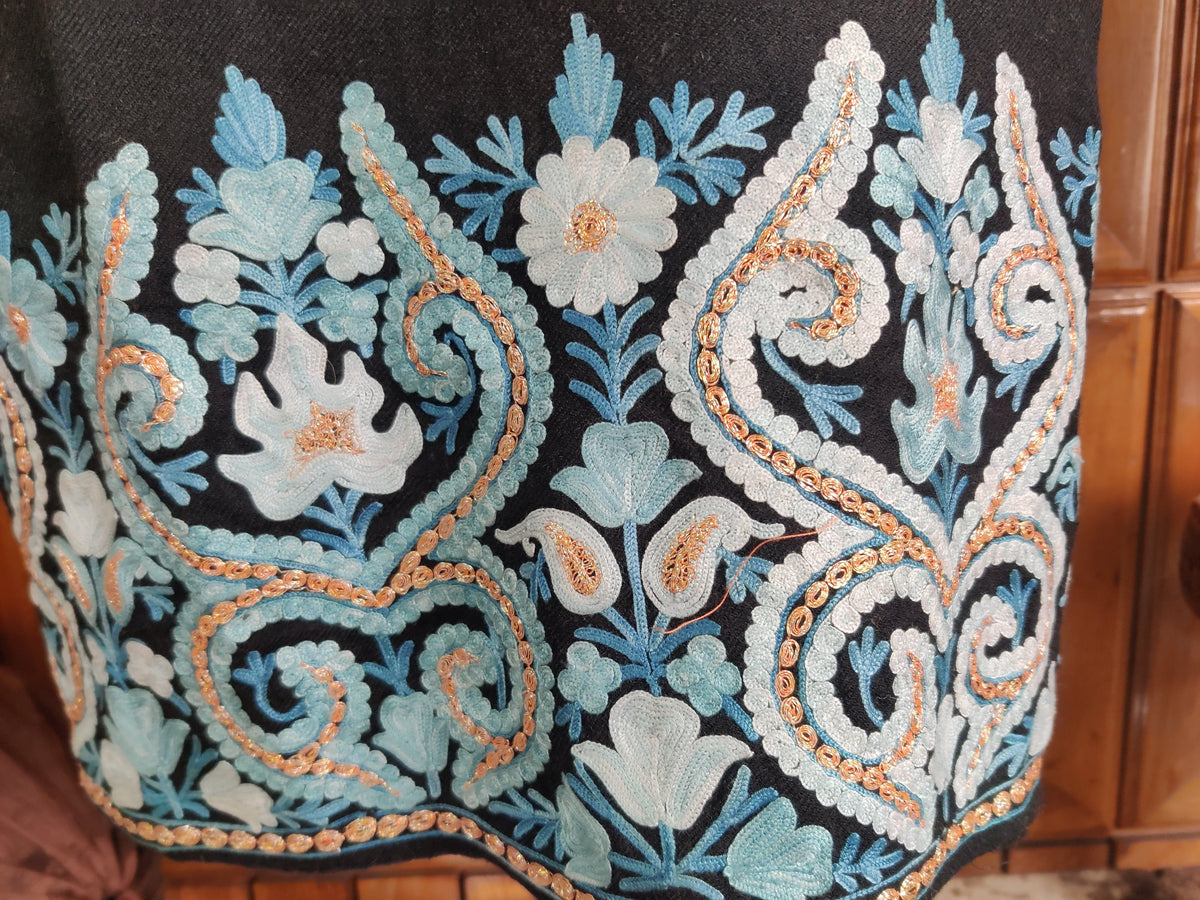 Close-up of blue and ivory paisleys and flowers with gold-toned accents on the black pheran border.