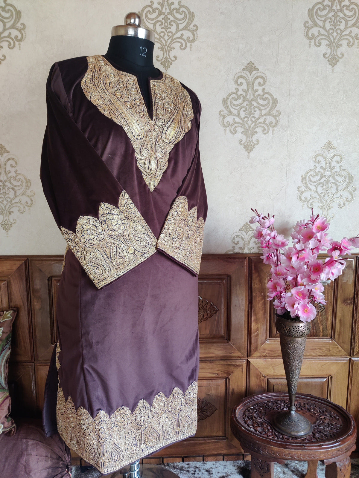 Angled front of a plum-burgundy velvet pheran on a mannequin, with gold-toned Tilla embroidery at the neckline, crossed cuffs and hem.