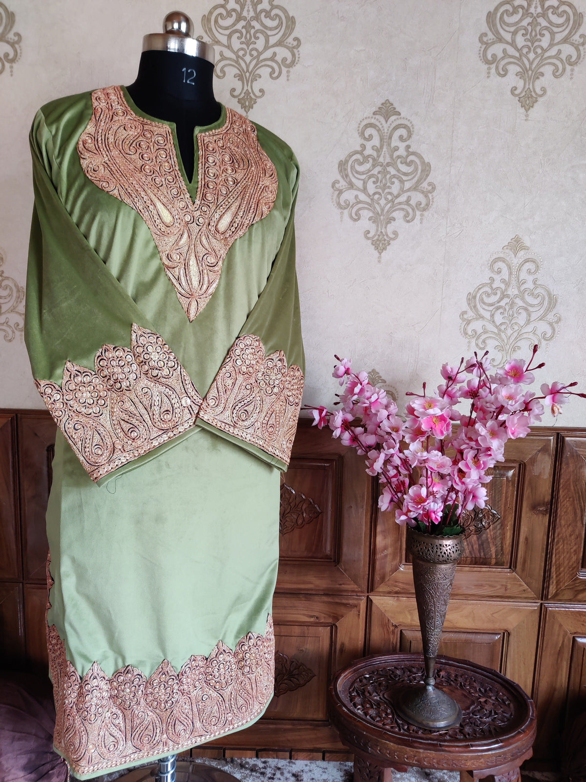 Full front view of a sage-green velvet pheran with copper-toned embroidered neckline, broad cuffs and a patterned hem.
