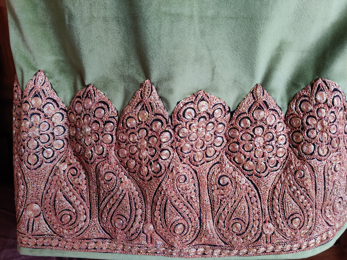 Copper-toned paisley and rosette border along the hem of the green velvet pheran.