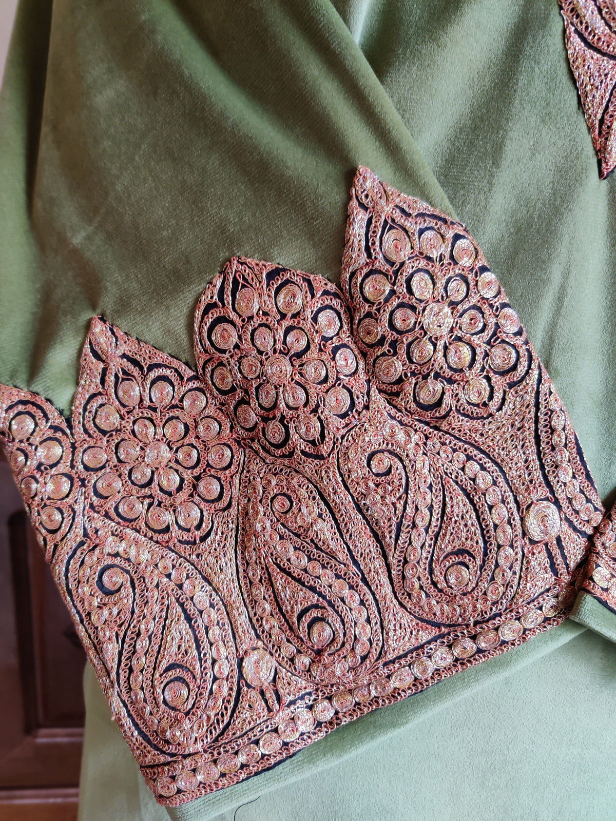 Close-up of a green velvet cuff with copper-toned paisleys and round floral motifs outlined in dark thread.