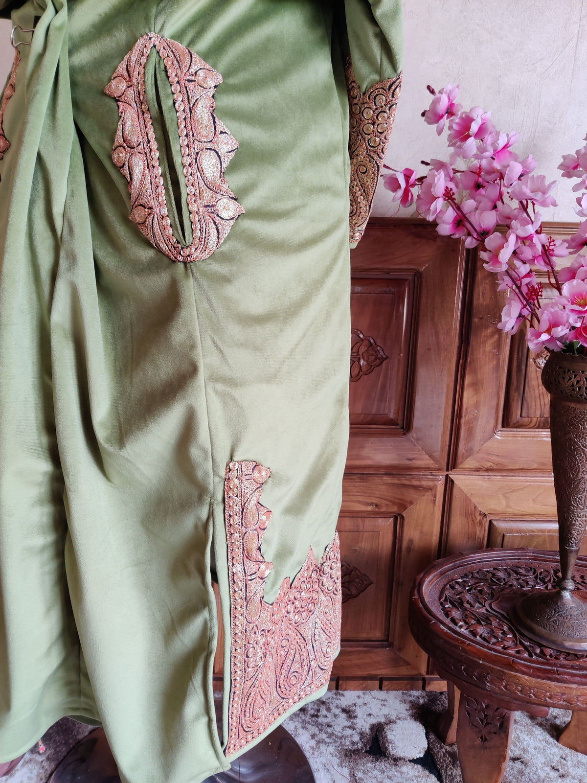 Side view of the green velvet pheran showing an embroidered pocket opening, side slit and copper-toned hem border.