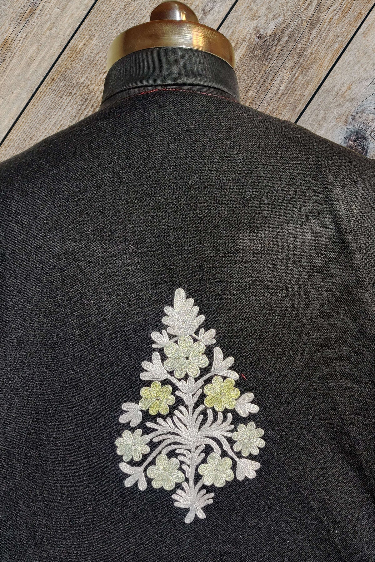 Close-up of a small cream and pale green Aari floral bouquet centred on the back of a black pheran