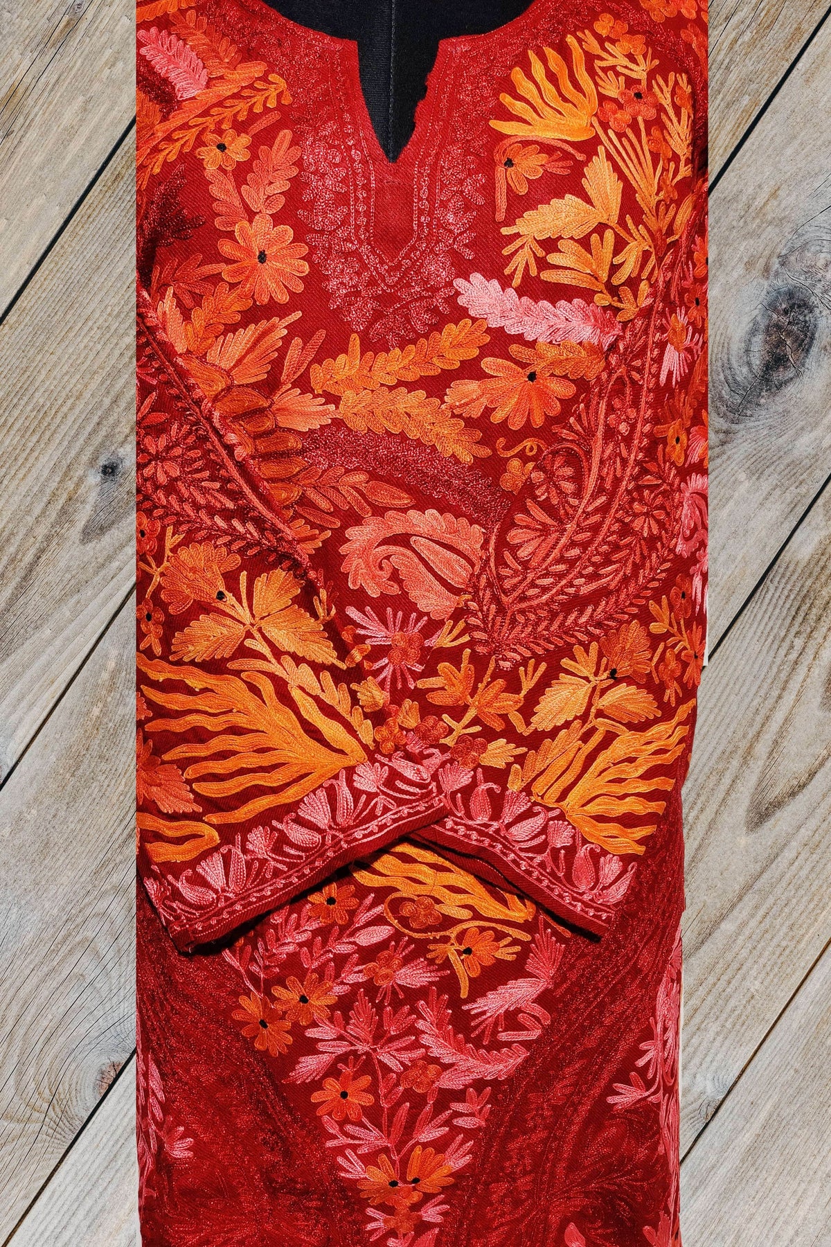 Front detail of a red pheran, showing dense orange and pink Aari-and-Zari floral embroidery, curling paisleys and crossed cuffs.