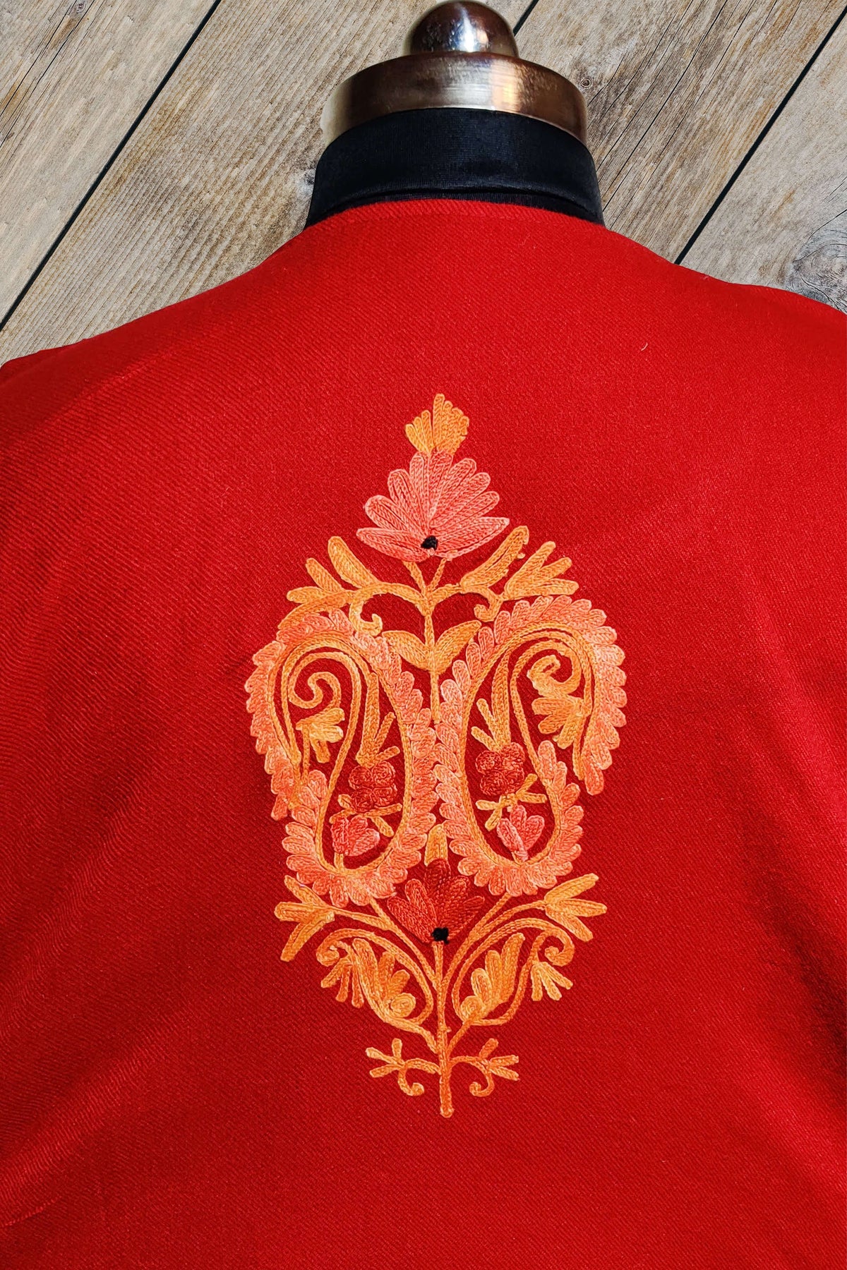Upper back of a red pheran on a mannequin, with a single orange and peach embroidered paired-paisley floral motif.