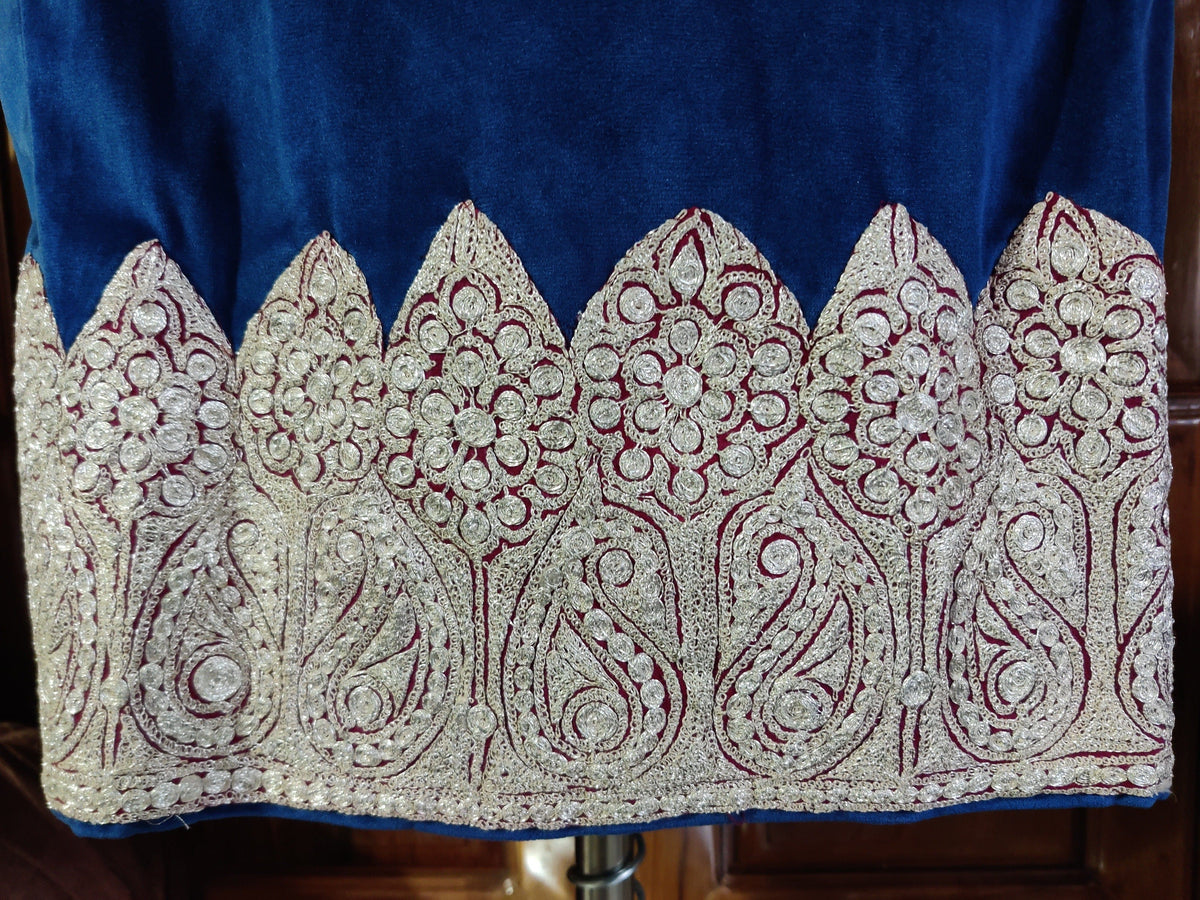 Close-up of a blue velvet pheran's hem, with silver-toned Tilla paisleys and round floral motifs inside pointed scalloped panels.