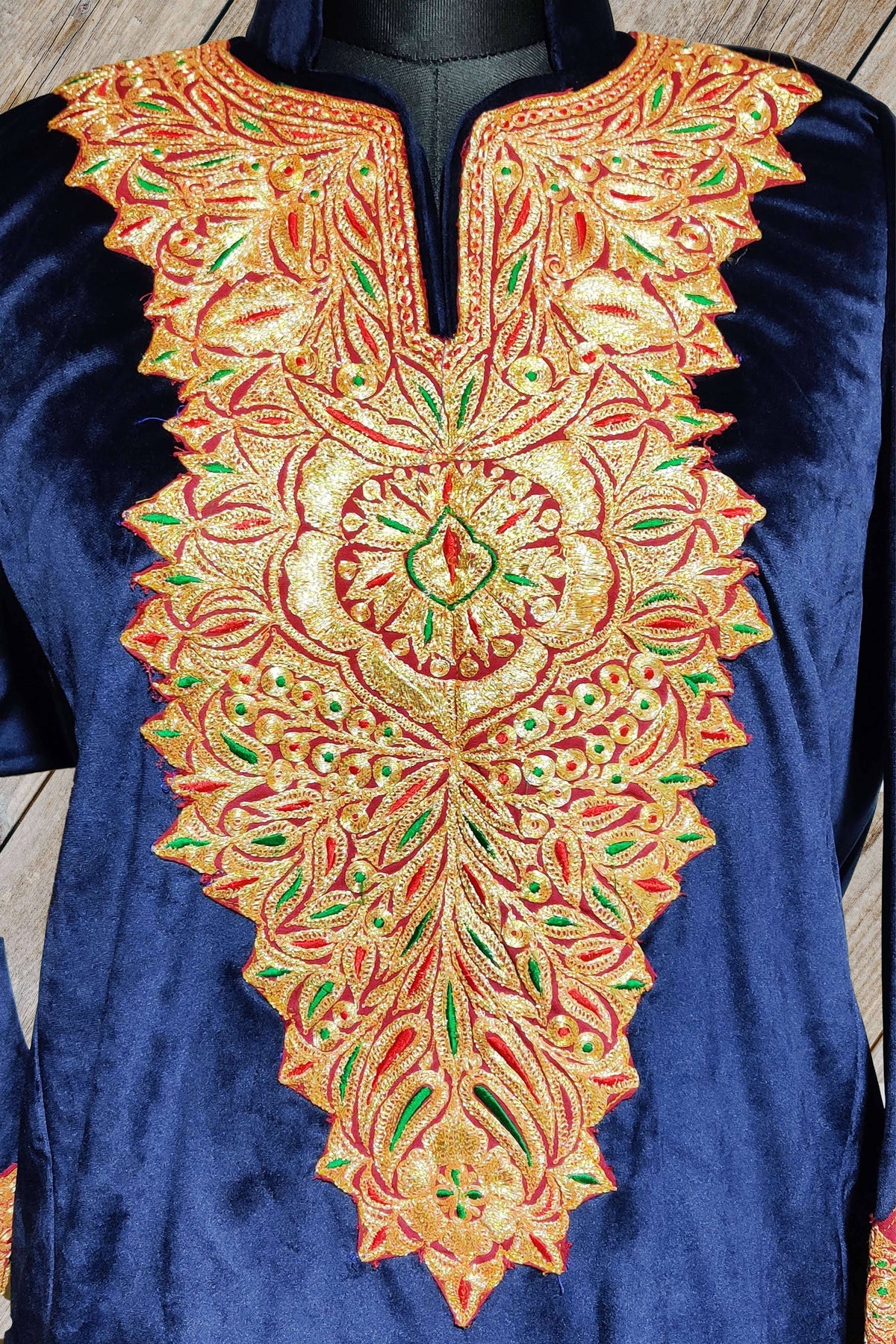 Close-up of the blue velvet pheran’s slit neckline and long gold-toned floral panel with red outlines and green details.