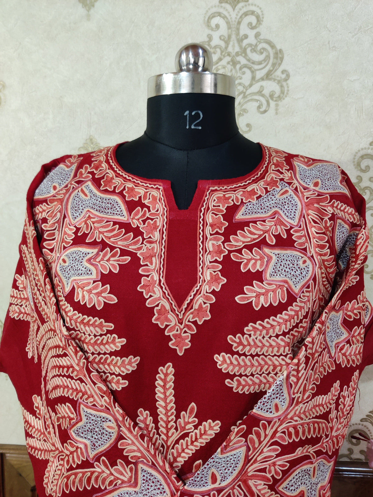 Upper front of a red pheran showing a long notched neckline framed by cream embroidery and pale blue floral motifs
