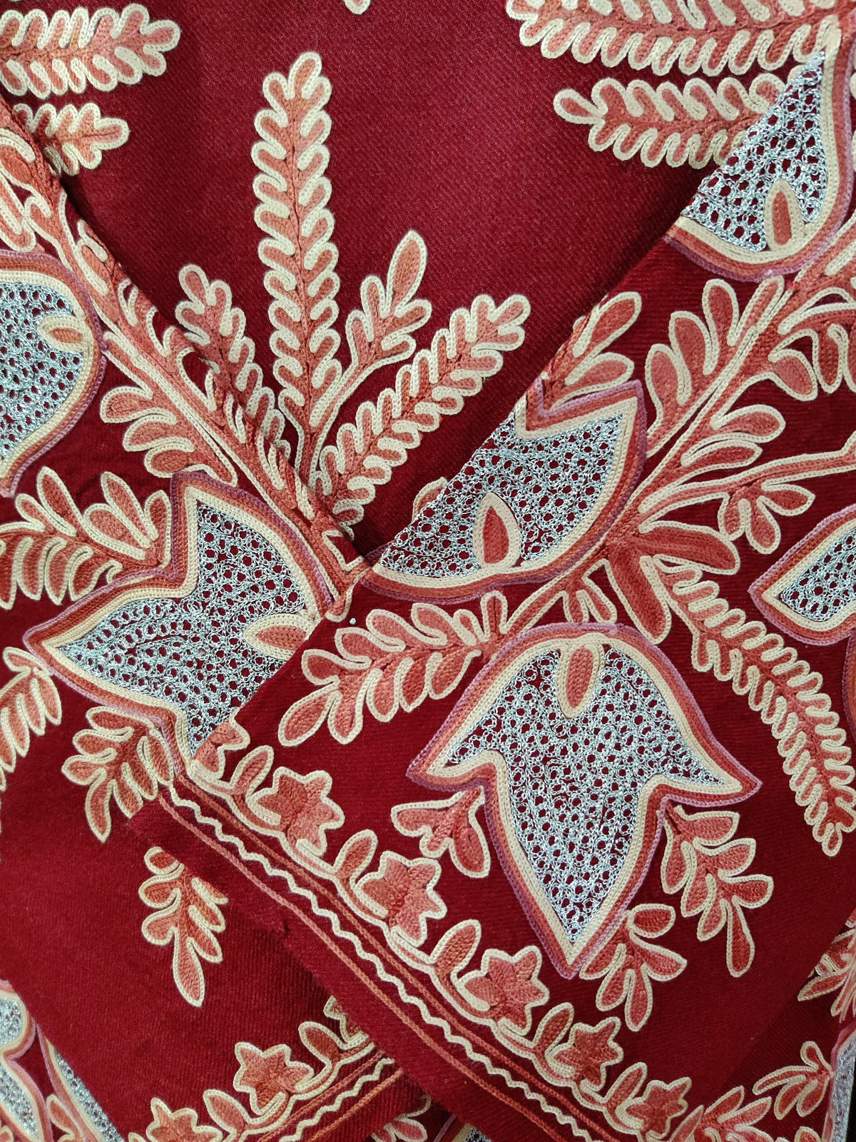 Close-up of crossed red pheran cuffs with cream Aari leaves and pale blue open-pattern Zari floral shapes