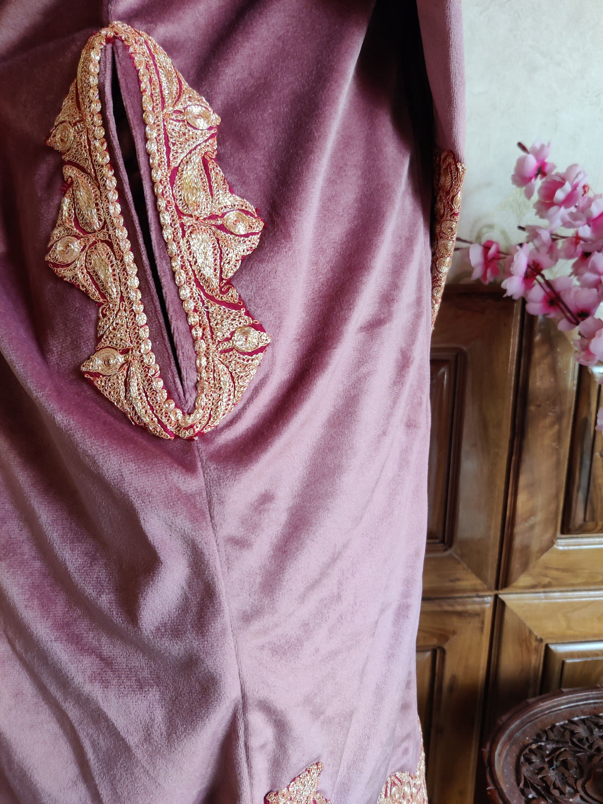 Pocket opening on a dusty pink velvet pheran framed by gold-toned Tilla leaves and narrow embroidered trim