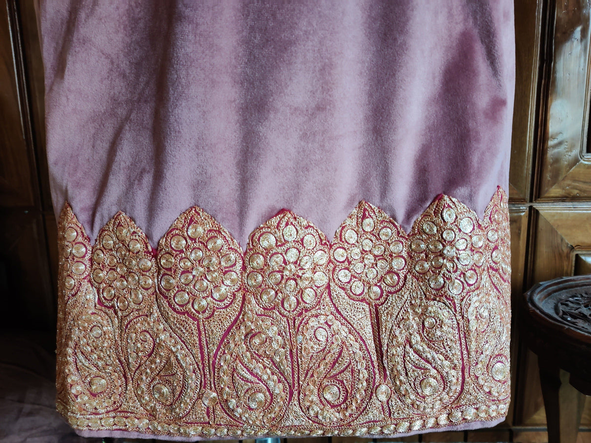 Hem detail of a dusty pink velvet pheran with repeating gold-toned Tilla paisleys and rosettes in pointed scalloped panels