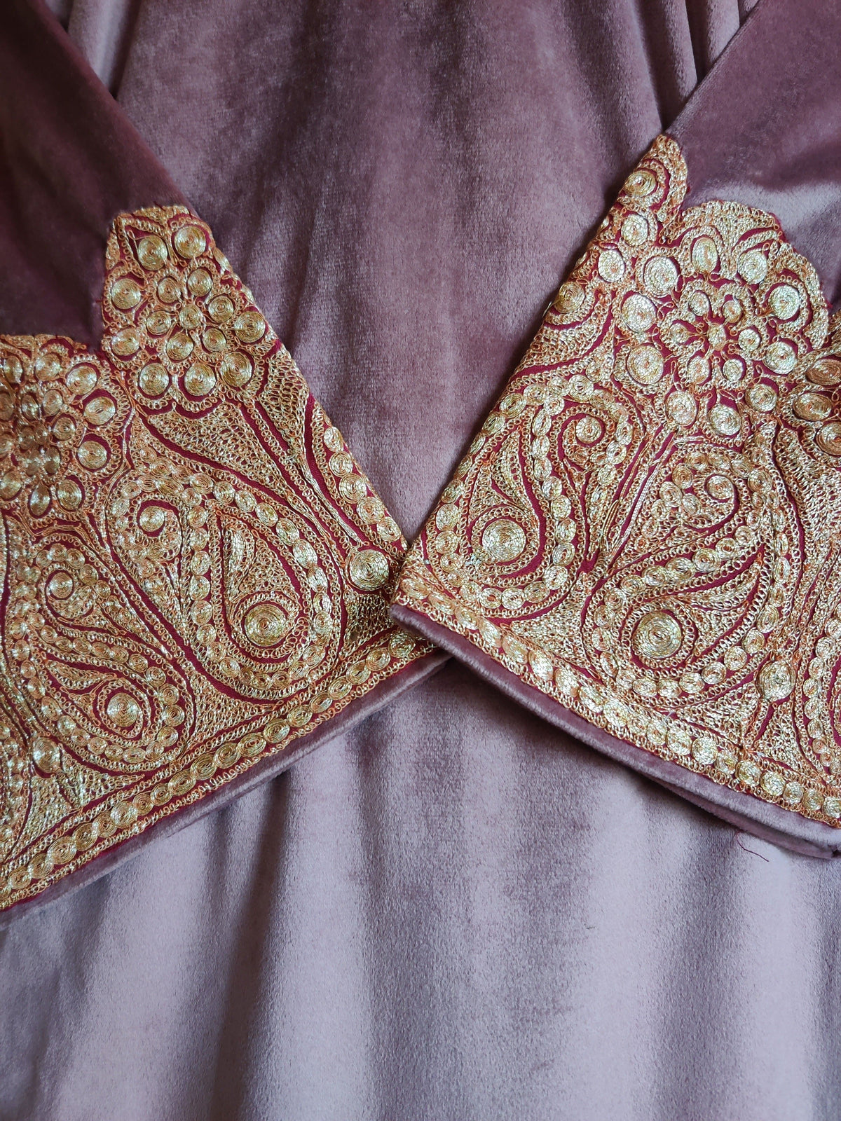 Close-up of crossed dusty pink velvet cuffs with gold-toned Tilla paisleys and round floral motifs