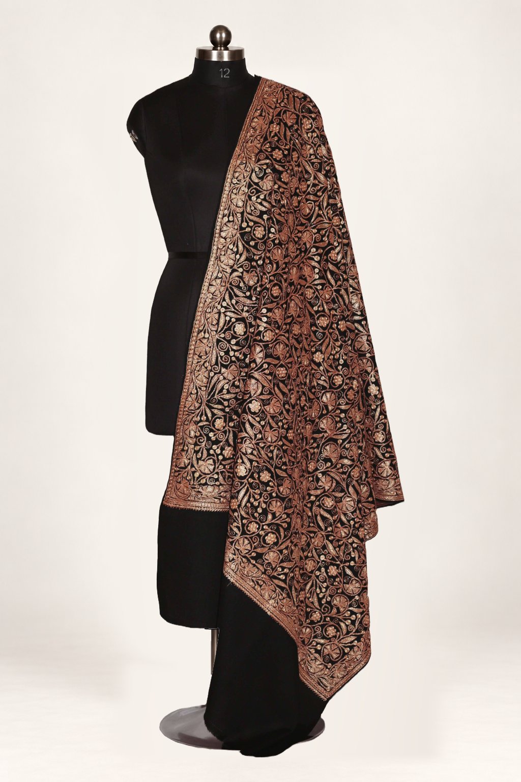 Black merino wool shawl draped over a mannequin’s shoulder, with dense copper-toned Tilla floral vines and a bordered edge