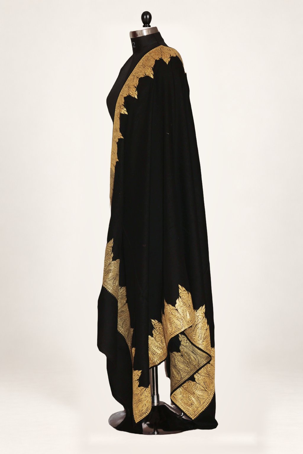 Side view of a black Merino wool shawl draped over a mannequin, showing gold Tilla edging and broad paisley borders at the hanging ends