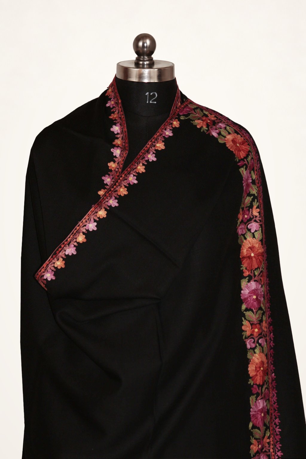Upper view of a black merino wool shawl wrapped on a mannequin, with red, pink and orange Aari floral borders and green leaves.