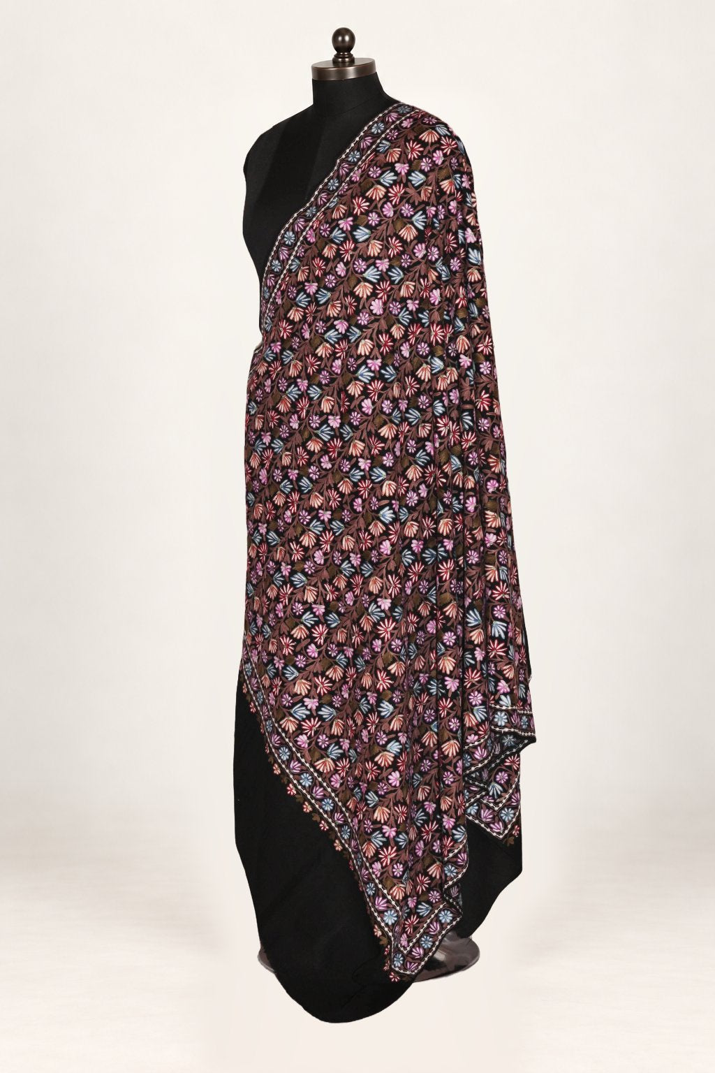 Black merino wool shawl draped over a mannequin’s shoulder, with dense small pink, blue and cream Aari flowers
