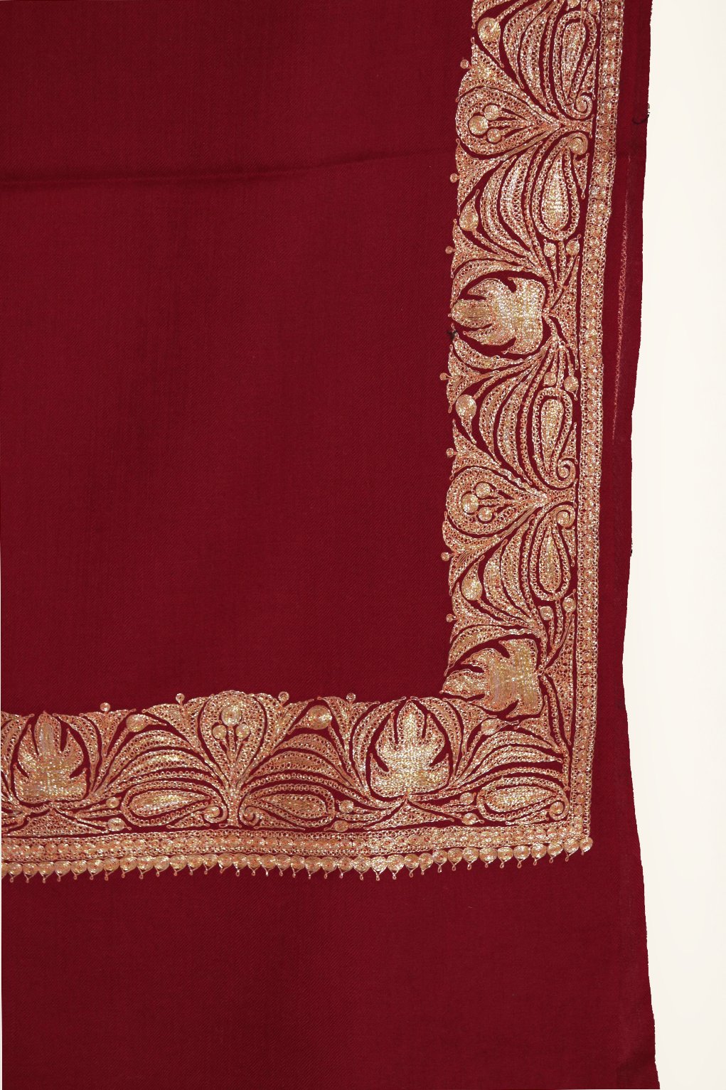 Close-up of a maroon Merino wool shawl corner with a gold Tilla border of curling leaves and paisley-shaped motifs